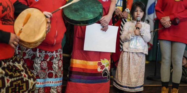 A child holding a microphone and surrounded by women wearing red
